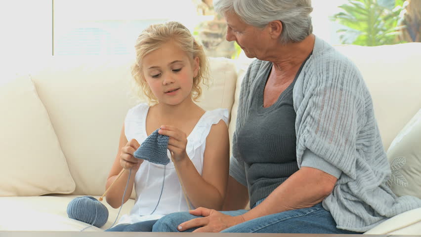 A little girl learning to knit with her Grandmother on a sofa