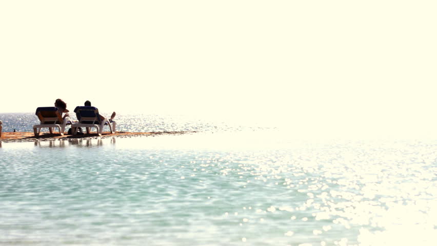 Two people sitting on sunbeds at the beach 