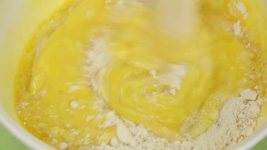 Preparing a cake mix by adding eggs, milk and butter then stirring with a wooden spoon. 