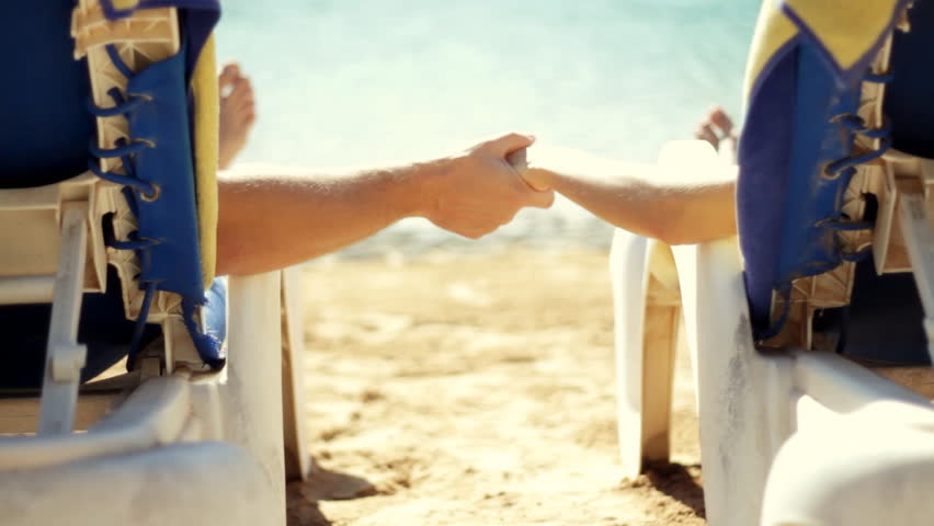 Couple lying in sunbeds holding hands by the water 
