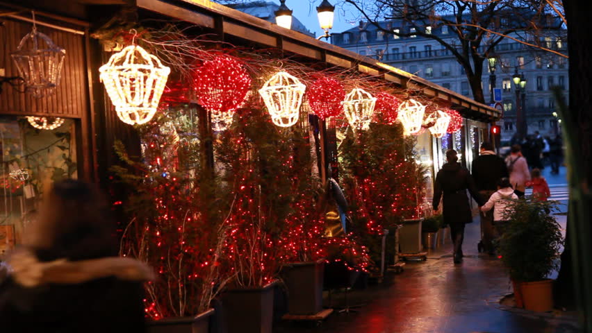 people walk at stalls with Christmas trees decorated lighted lanterns and illuminated in Paris evening