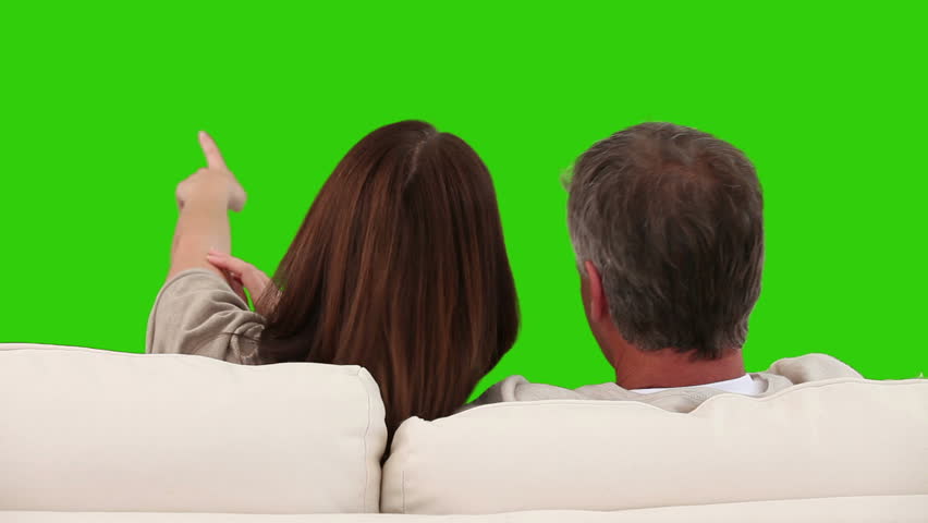 Retired couple watching tv on a sofa against a green screen