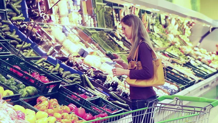Woman in a supermarket at the vegetable shelf shopping for groceries, he is checking out the groceries