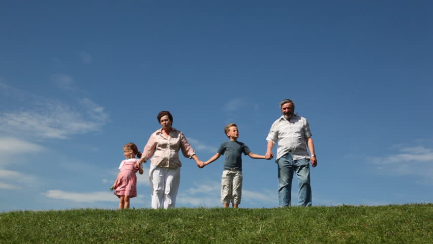 happy grandparents and grandchildren holding hands stand on grass, then run away 