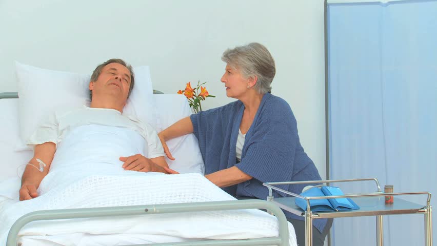 Man lying on his back receiving a visit from his wife at the hospital