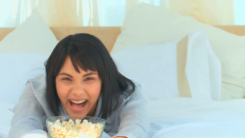 Casual asian woman watching tv with popcorn in the bedroom