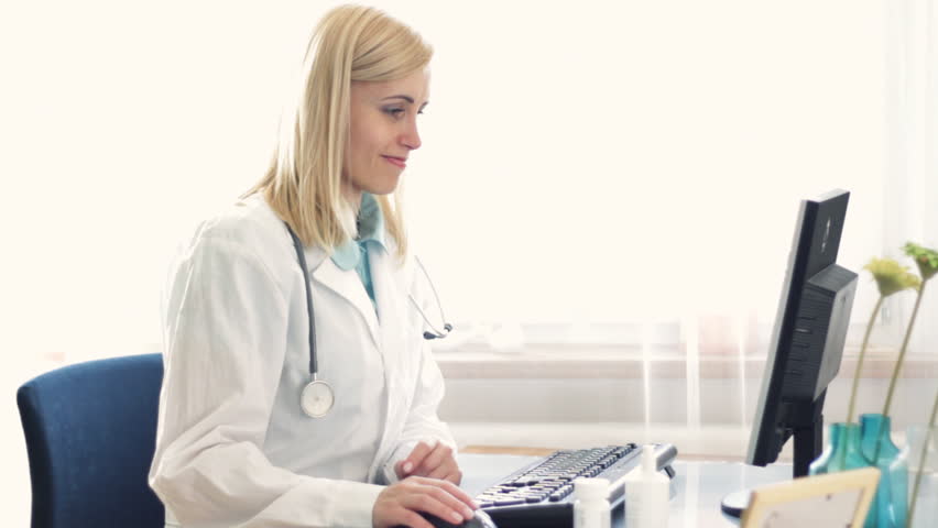 Female doctor working on computer and checking pills bottle 