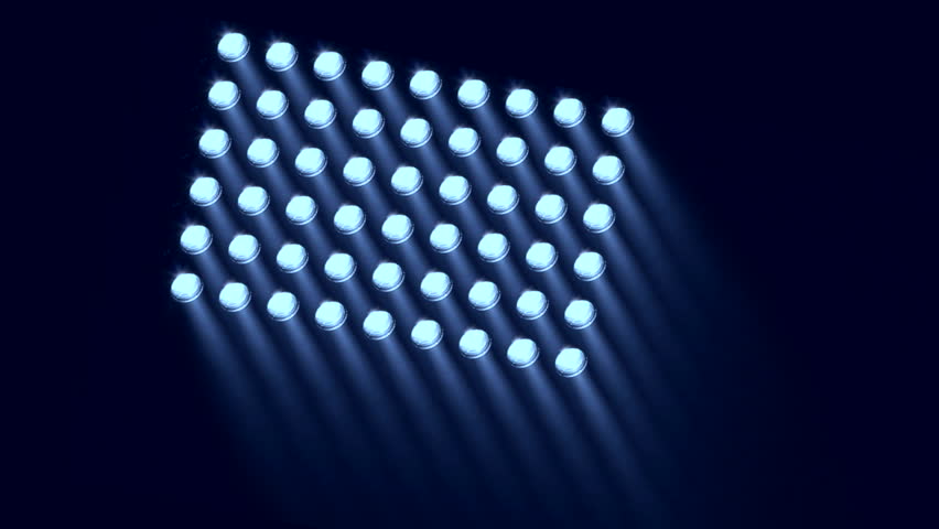 A baseball is illuminated by stadium lights as it sits in the grass, and the lights come on one by one.