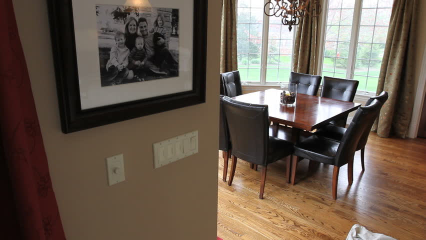 Moving dolly shot of a breakfast nook table and chairs surrounded by large windows in a luxury home, with a family portrait on the wall