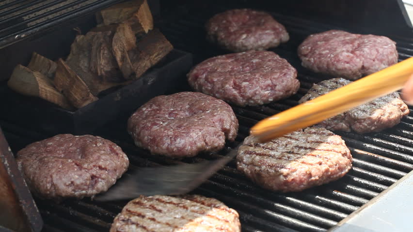 A barbecue scene with chicken meat, burgers and sausages while flipped over with a tong spatula turner  on the grill over a calm fire flame.