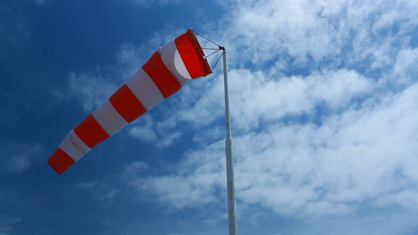 wind sock - red and white pointer indicating strength and direction of the wind against the blue sky with fluffy clouds