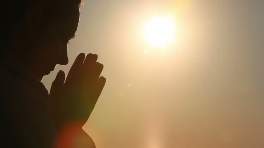 Silhouette of woman head with sunshine behind, holding hand in namaste