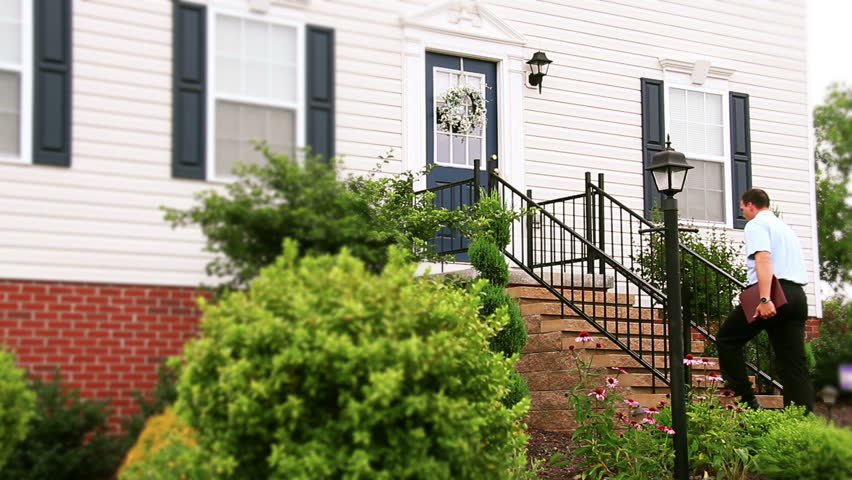 A door to door salesman walks up to a house and knocks on the door.