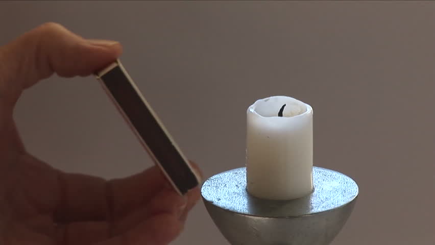 Close up of match being struck against a match box then lighting a candle. 