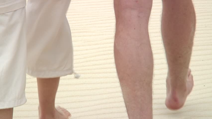 Couple walking barefoot in the sand of a beach.