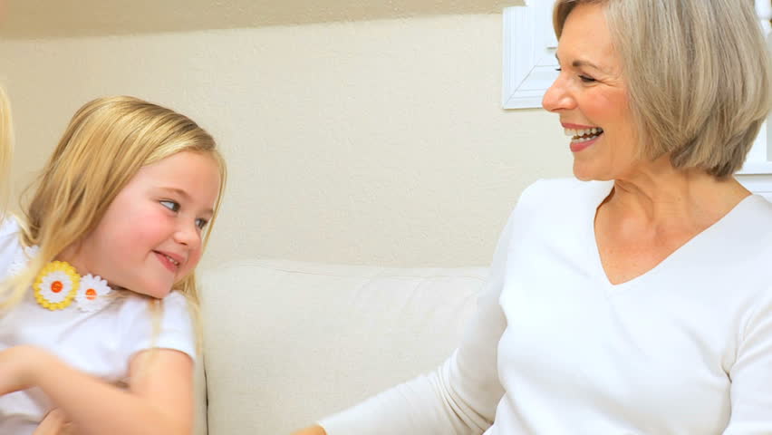 Grandma cuddling her cute little grand-daughter on sofa at home visit
