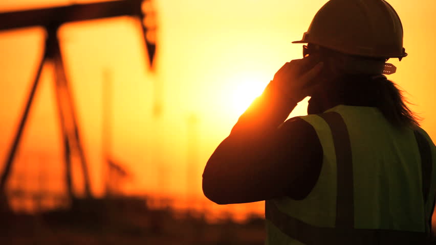 Female engineer using a cell phone overseeing the site of crude oil production at sunset