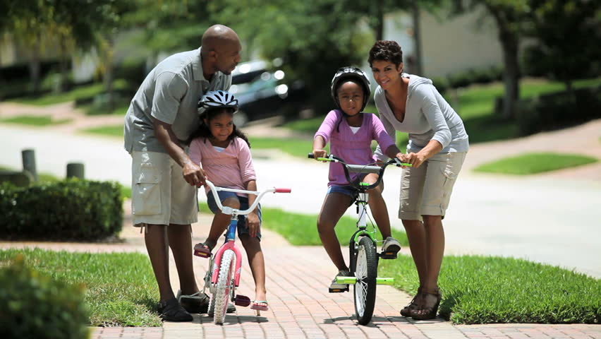Little african american girls being helped to ride a bicycle by her parents