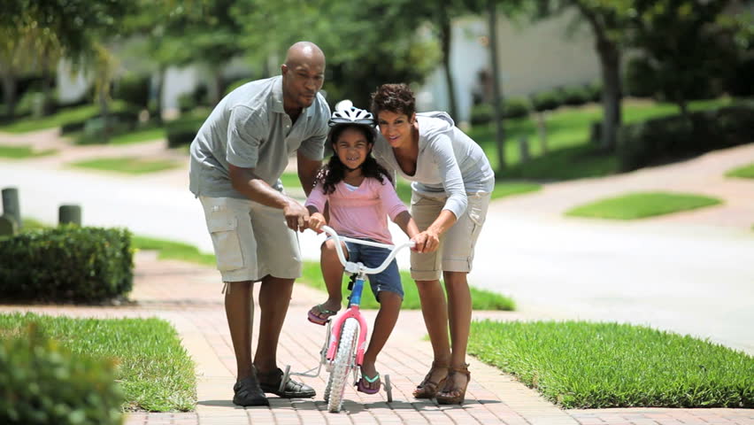 Little african american girl being helped to ride a bicycle by her parents
