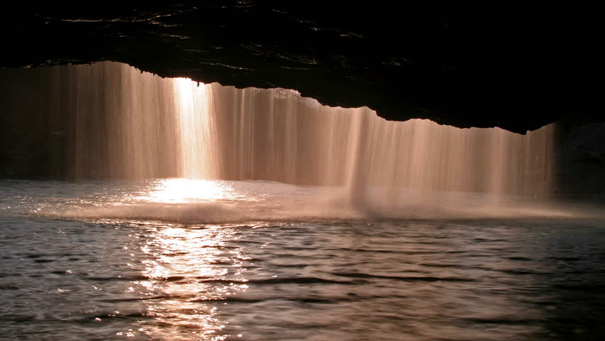 Sun shining behind the waterfall in a river cave