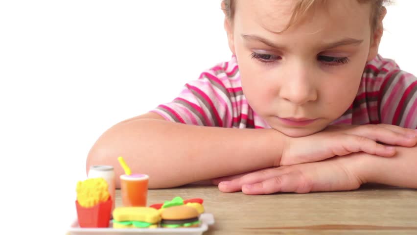 Sad little girl sitting with her head on her hands and looking at artificial copy of fast food 