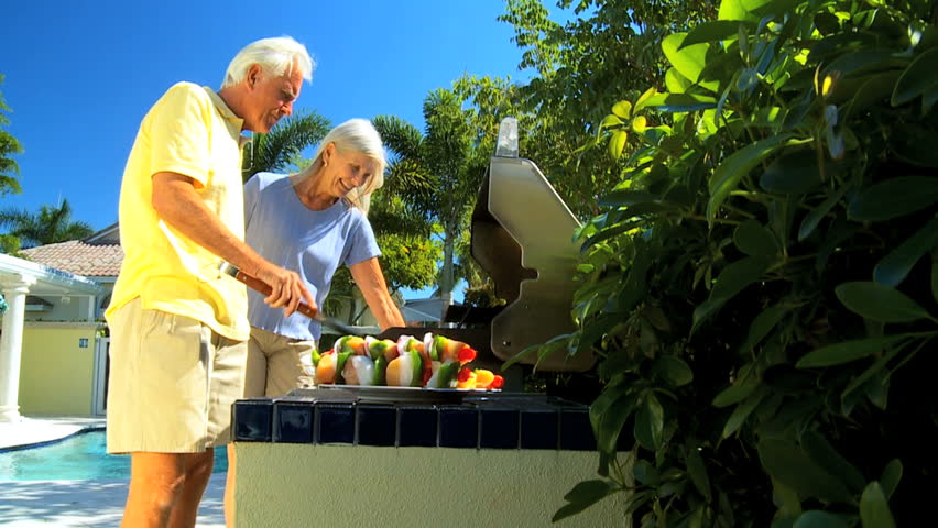 Senior couple enjoying a healthy eating lifestyle grilling delicious fresh food on a barbecue outdoors filmed at 60FPS