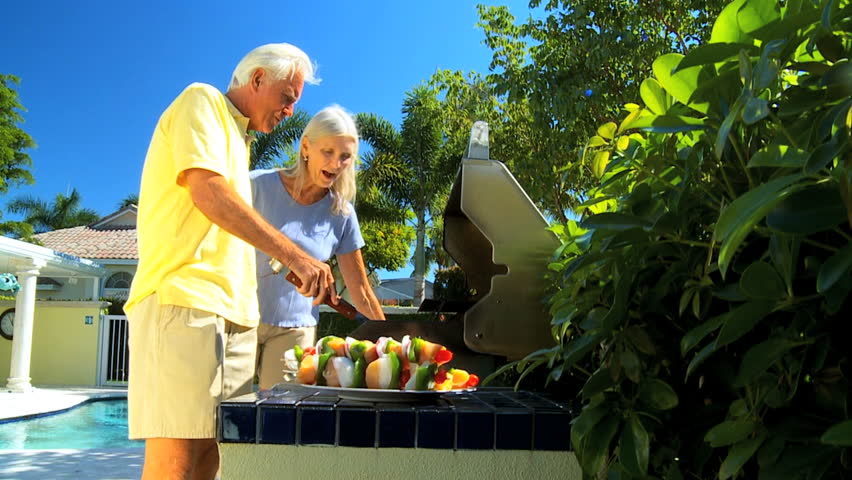 Senior couple enjoying a healthy eating lifestyle grilling delicious fresh food on a barbecue outdoors filmed at 60FPS