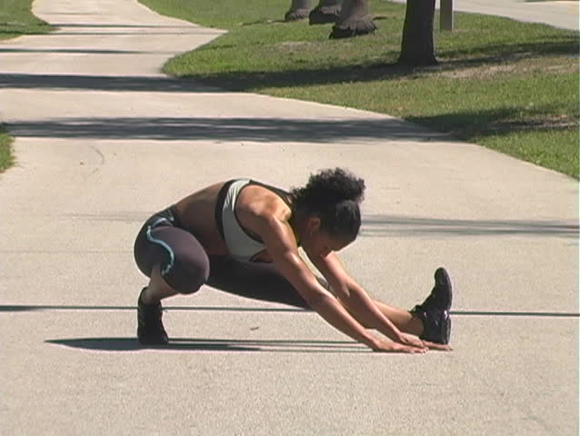 A beautiful woman stretches on a jogging track before running on a bright, sunny day.