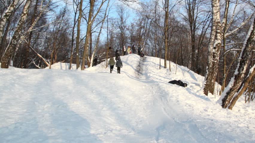 Boy slid down slope and rolled over, several people stand on hill at sunny winter day