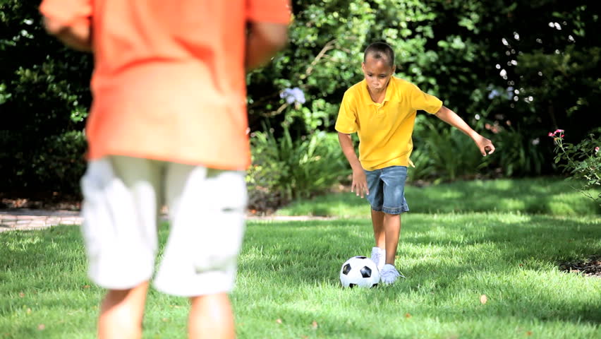 African american father & son kicking a ball together in the park