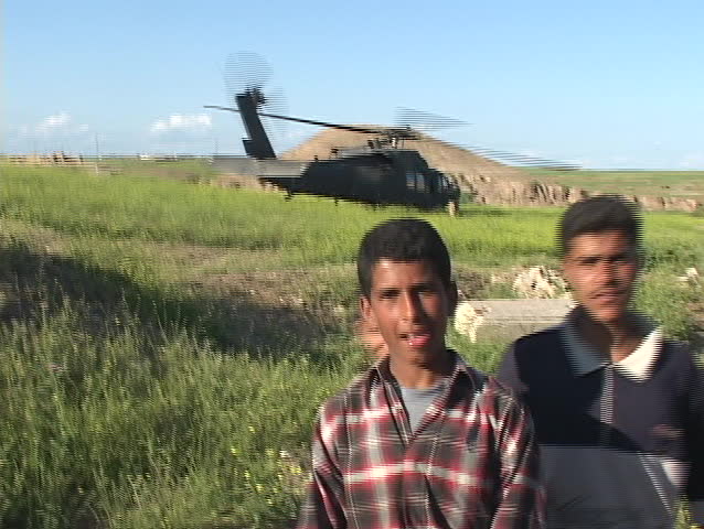 IRAQ - CIRCA 2003: Iraqi boys pose and give peace signs in front of a Blackhawk helicopter circa 2003 in Baghdad.