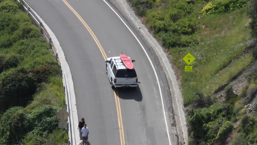 SUV with surfboard on top, driving up from beach access