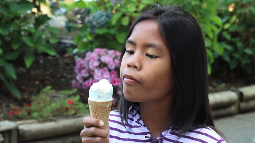 A cute 9 year old Asian girl enjoys a delicious ice cream cone during the summer.