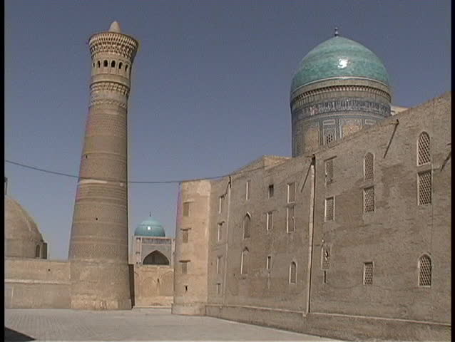 Birds fly around the ancient Kalyan Minaret and two turquoise mosque domes.