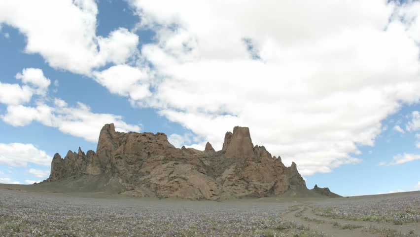 Sunlight reflects in patches as fluffy white clouds pass over New Mexico's Shiprock.
