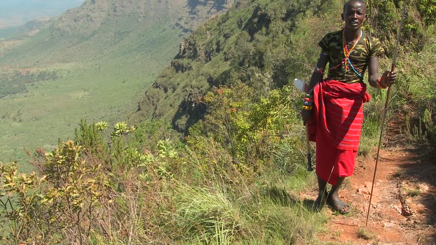 KENYA - CIRCA 2009: Tilt up to reveal a Masai warrior standing at the edge of a vast canyon circa 2009 in Northern Kenya.