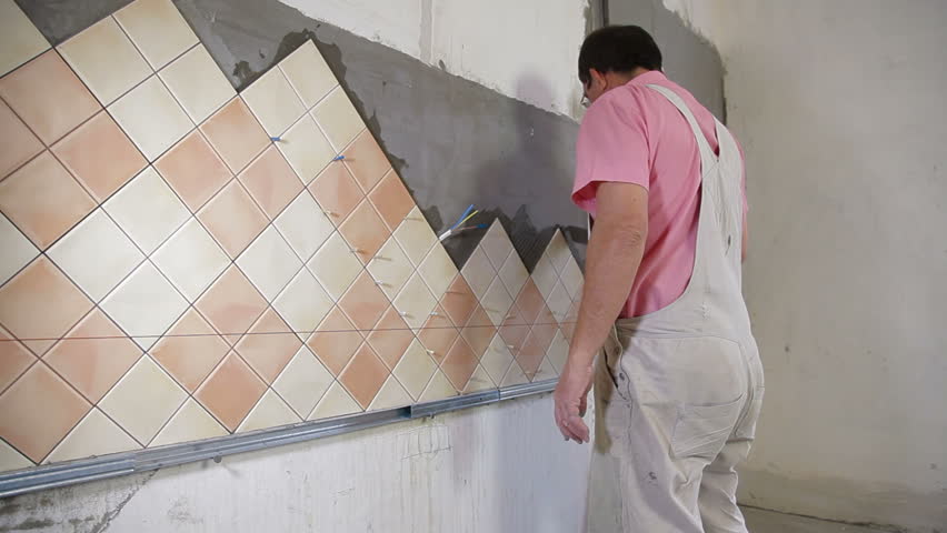 man applying ceramic tile to a Kitchen wall, working with trowel