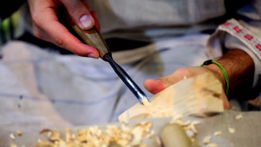 Carver cuts a wooden toy and compares it with other, only hands visible