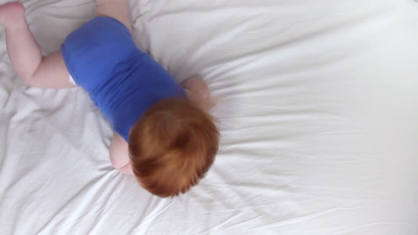 HD: Top down happy crawling baby Red hair baby laughing while he crawls. The small boy looks at the viewer and crawls over the white bed.