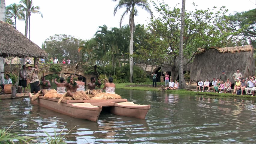 Polynesian Cultural Center in Laie Oahu Hawaii. Canoe show with dancers from Fiji. Demonstration for tourists in the main lagoon. Splashing weapons in river. Water, lagoon and palm trees.