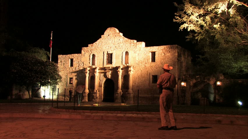 The historic Alamo at night. Ranger police officer. Spanish Mission and location of the battle with Santa Anna of Mexico for Texas independence. Tourists walking.