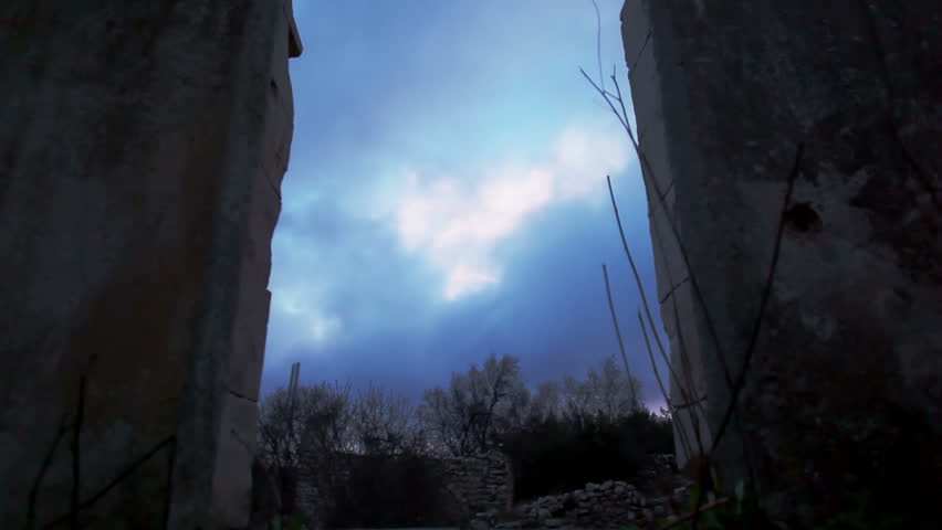 The sun trying to shine through the turbulent clouds at dusk at the Bar'am ancient ruins in Israel.  The shot is taken between two silhouetted pillars.
