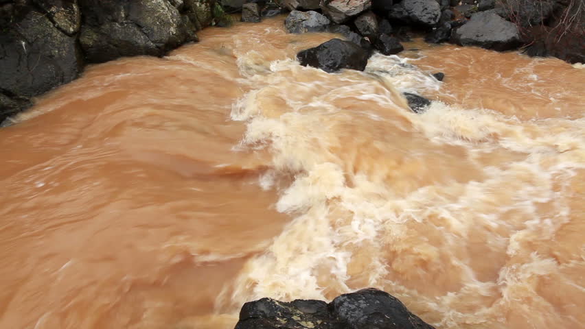 Close-up of a small, turbulent rapid of muddy water at a river in the Golan Heights, Israel.  The rocks under the water cause this disturbance of silted water.