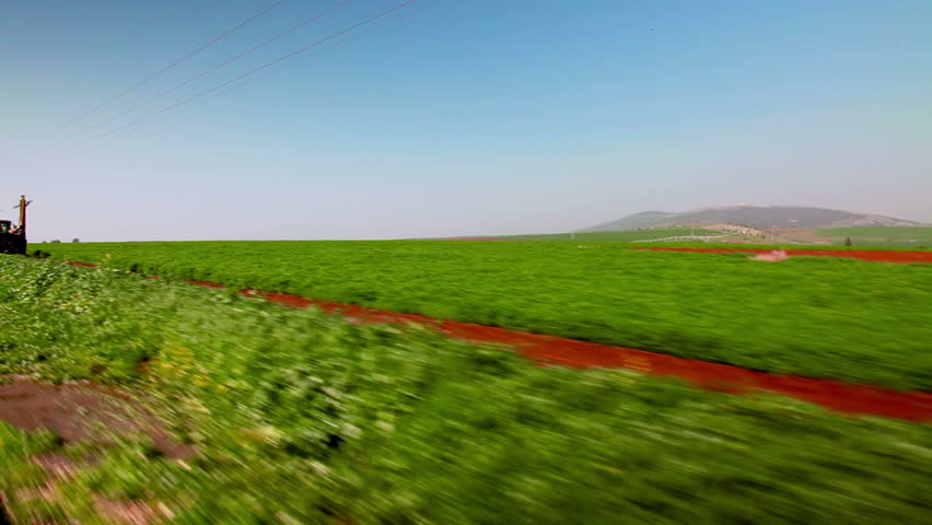 Drive-by in the Ein Harod farmland region of Israel showing a lush green field.  As we move along a tractor is driving in the field that we pass.