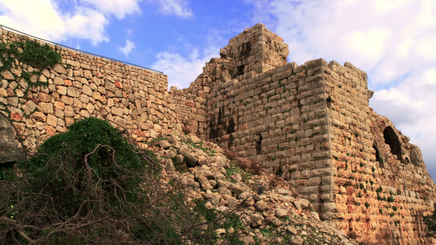 Slow pan, looking up, across the base of the Nimrod Fortress in the Golan Heights, Israel, with fluffy clouds in the sky.  02/21/2011