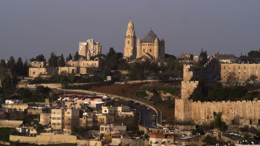 Wide shot of Hagia Maria Sion Abbey on Mt. Zion and the south end of the old city wall in Jerusalem, Israel. Just below the Benedictine abbey is a parking lot filled with tourist buses.  02/26/2011