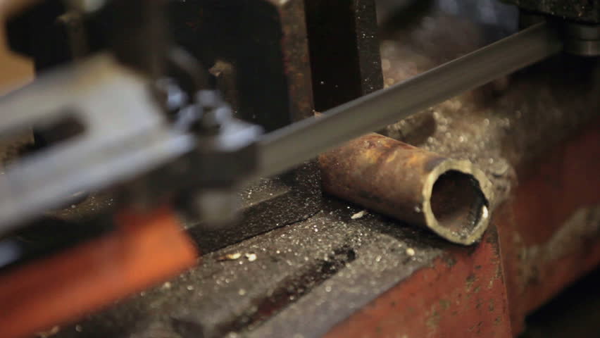 Cutting a hard steel pipe held in vise by heavy duty band saw. Industrial manufacture.