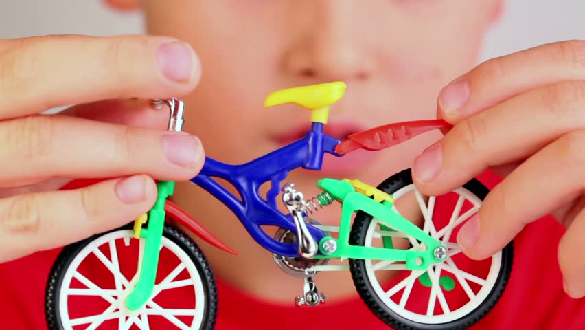 Boy hold toy bike in front of his face, he pushes and moves some parts