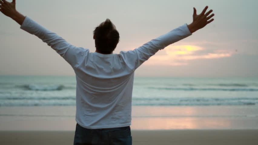 Man at the beach raising hands to the sky, freedom concept