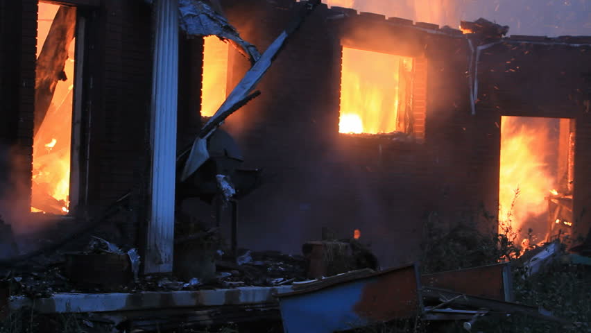 House burning with intense flames after dark. Flames and smoke coming from windows and doors. Total loss and destruction.